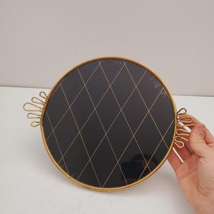 May include: A round gold tray with a black diamond pattern on the bottom. The tray has two gold handles on the sides.