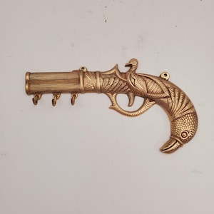 May include: A gold-toned metal key holder shaped like a pistol with a bird design. The holder has five hooks for keys.