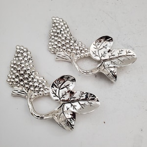 Peut inclure: Deux objets décoratifs argentés en forme de grappe de raisin et de feuilles. Chaque pièce présente une grappe de petits raisins ronds et des feuilles détaillées. Les feuilles ont des motifs de veines complexes. Les objets sont probablement des éléments décoratifs.