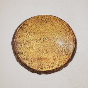 K&ouml;nnte beinhalten: Ein rundes Holztablett mit gelber Beize und einem dunkelbraunen Rand. Das Tablett hat eine raue, strukturierte Oberfl&auml;che und eine kreisf&ouml;rmige Vertiefung in der Mitte.