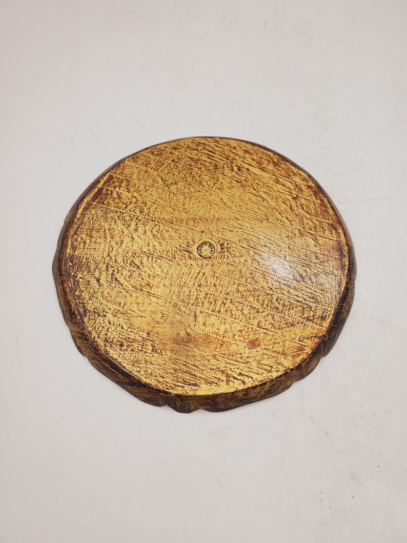 K&ouml;nnte beinhalten: Ein rundes Holztablett mit gelber Beize und einem dunkelbraunen Rand. Das Tablett hat eine raue, strukturierte Oberfl&auml;che und eine kreisf&ouml;rmige Vertiefung in der Mitte.