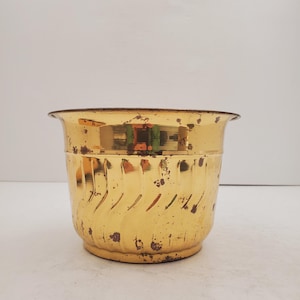 May include: A gold metal planter with a decorative swirl pattern. The planter has a slightly worn look.