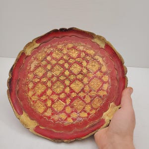 K&ouml;nnte beinhalten: Ein rundes, rotes Tablett mit goldfarbenem Rand und einem dekorativen Muster aus gelben Blumen und Diamanten.