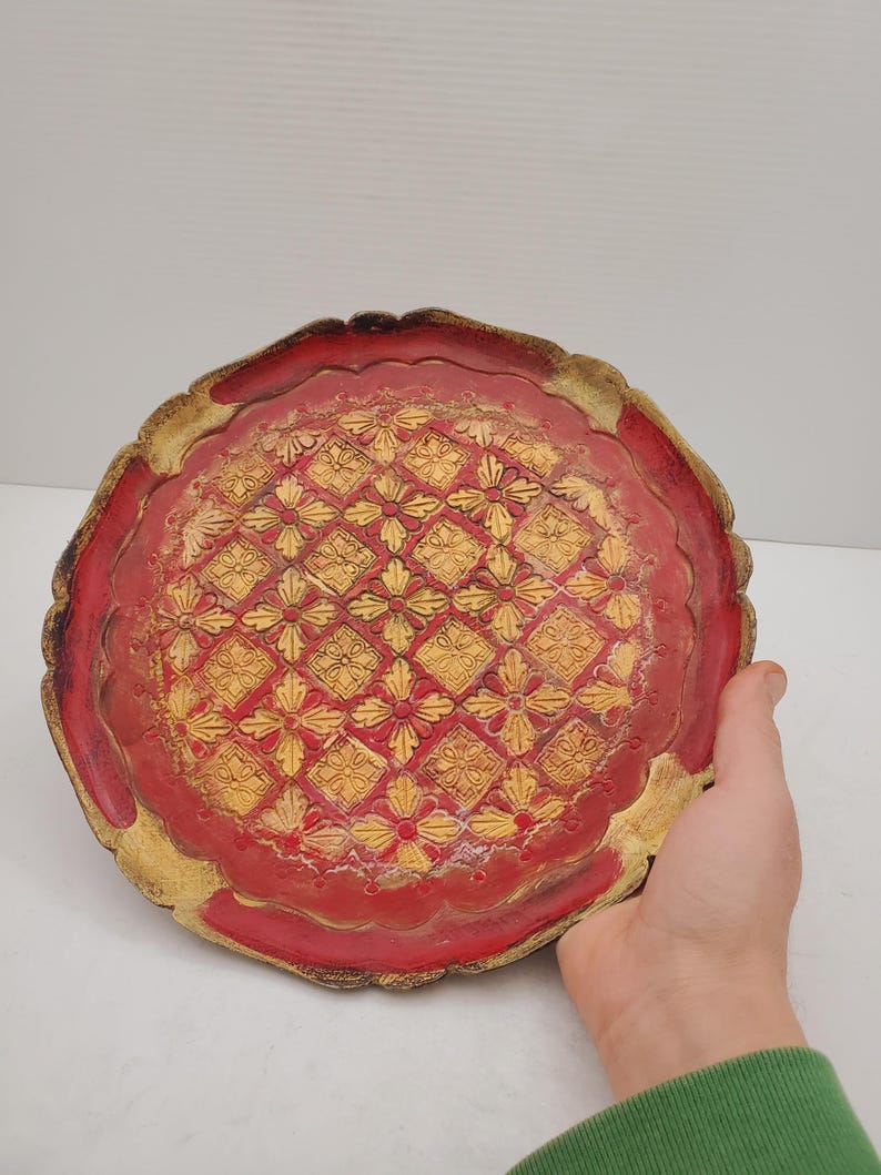 K&ouml;nnte beinhalten: Ein rundes, rotes Tablett mit goldfarbenem Rand und einem dekorativen Muster aus gelben Blumen und Diamanten.