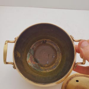 May include: A brass pot with a lid. The pot has two handles and a round bottom. The inside of the pot is tarnished.