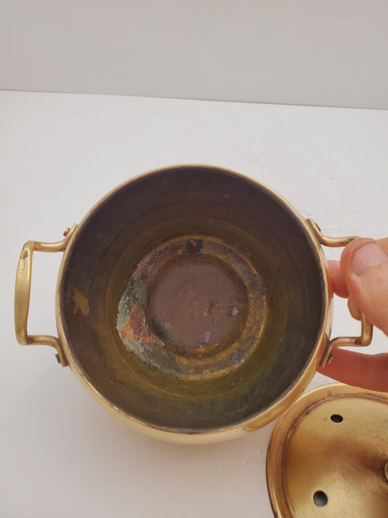 May include: A brass pot with a lid. The pot has two handles and a round bottom. The inside of the pot is tarnished.