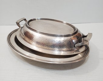 May include: A silver oval serving dish with a hammered finish and a lid. The lid has two handles and the dish has a raised rim.