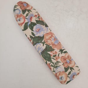 Peut inclure: Une housse de planche à repasser à motifs floraux. La housse présente un fond crème avec de grandes fleurs dans les tons pêche, bleu et vert. La housse est oblongue et a une extrémité arrondie.