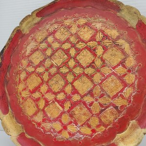 K&ouml;nnte beinhalten: Ein rundes, rotes Holztablett mit einem goldfarbenen Design aus Blumen und geometrischen Formen. Das Tablett hat einen gewellten Rand.