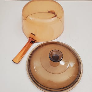 May include: A brown glass saucepan with a lid. The saucepan has a handle and the lid has a knob.