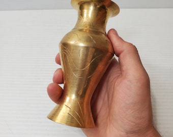 May include: A small, brass vase with a flared base and a slightly wider top. The vase has a smooth, polished surface with etched, curved lines. The overall shape is elegant and the brass has a warm, golden colour. The vase is approximately 15 cm tall.