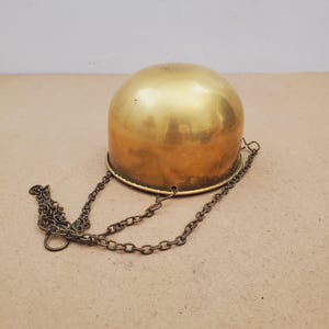 以下が含まれることがあります： 磨き上げられた真鍮製のドーム型ボウルで、3本の細い金属チェーンで吊り下げられています。ボウルは滑らかで光沢のある金色をしており、底は丸みを帯びています。チェーンは縁に沿って等間隔に配置されたポイントに取り付けられています。