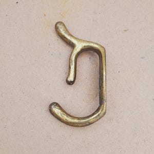 May include: A dual-pronged wall hook crafted from aged brass with a weathered, metallic finish. The hardware features a vertical mounting plate with two curved hooks extending outward, designed for hanging items securely on a flat surface.