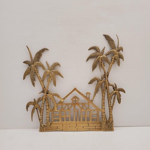 Peut inclure: Une décoration murale en métal doré représentant une maison découpée avec des palmiers de chaque côté. La maison a un toit, des fenêtres et une porte. Les palmiers ont des troncs et des feuilles.