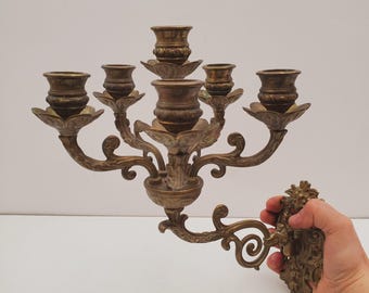 Könnte beinhalten: Ein Wand-Kandelaber aus Messing mit fünf Kerzenhaltern. Der Kandelaber hat ein dekoratives, verziertes Design mit Schnörkeln und floralen Motiven. Es ist ein Stück im Vintage-Stil.