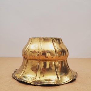 May include: A vintage brass decorative object with a flared, fluted design. The object has a wide base and a narrower top, with a golden finish and signs of age. The piece is likely a decorative element or part of a larger item.