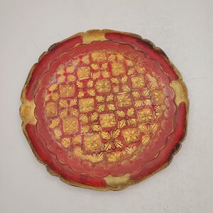 K&ouml;nnte beinhalten: Ein rundes, rotes Holztablett mit einem goldfarbenen Design aus sich wiederholenden Quadraten und Blumen. Das Tablett hat einen gewellten Rand.