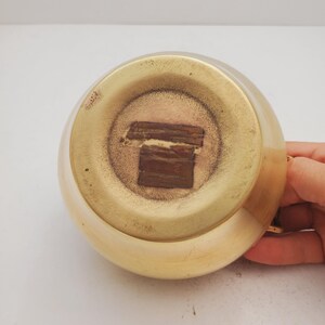 May include: The bottom of a gold-colored metal pitcher with a brown sticker on the bottom.