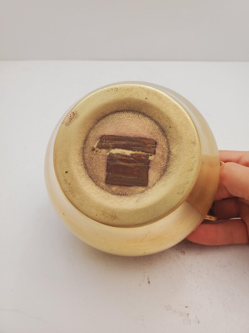 May include: The bottom of a gold-colored metal pitcher with a brown sticker on the bottom.