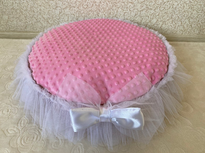 May include: A pink and white pet bed with a white tulle ruffle and a white satin bow. The bed is made of soft, plush fabric with a dotted pattern.