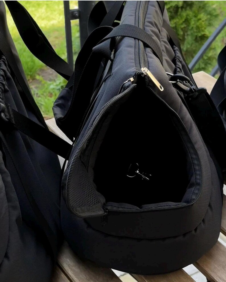 Puede incluir: Bolsa de transporte para mascotas negra con una abertura con cremallera y un panel de malla. La bolsa tiene un asa y una correa para el hombro.