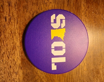 May include: A purple round coaster with the word "SOILS" in white letters and a yellow outline of the state of Minnesota.