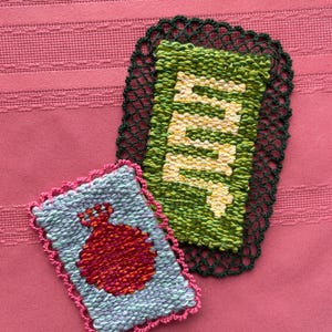 May include: Two handmade woven coasters. One is light blue with a red pomegranate design and a pink crocheted border. The other is green with the word "Mint" woven in yellow and white, with a dark green crocheted border.