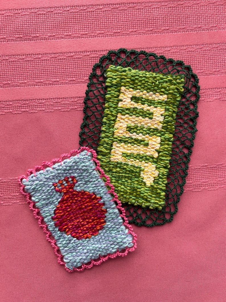 May include: Two handmade woven coasters. One is light blue with a red pomegranate design and a pink crocheted border. The other is green with the word "Mint" woven in yellow and white, with a dark green crocheted border.