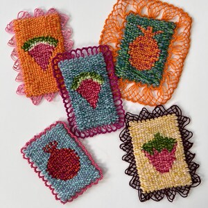 May include: Five colorful, woven textile art pieces. Each piece features a fruit design, including strawberries and pomegranates, with a scalloped lace border. The pieces are in shades of orange, blue, green, and yellow, with pink and brown lace.