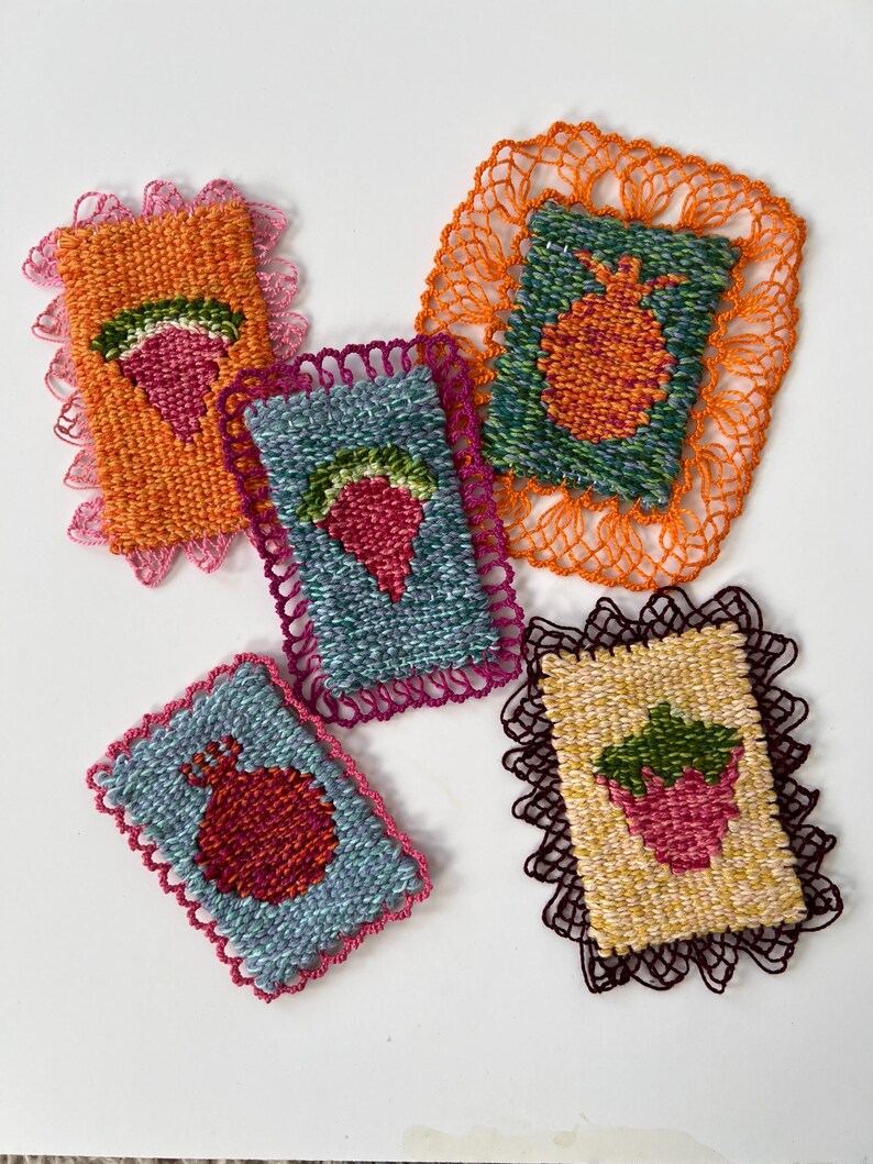 May include: Five colorful, woven textile art pieces. Each piece features a fruit design, including strawberries and pomegranates, with a scalloped lace border. The pieces are in shades of orange, blue, green, and yellow, with pink and brown lace.