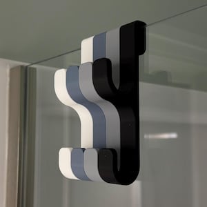 Puede incluir: Tres ganchos en blanco, gris y negro, diseñados para colgar sobre una puerta o estante de vidrio.
