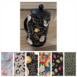 Può includere: Una caffettiera a pistone nera con una copertura in tessuto nero e marrone. La copertura in tessuto ha un tema caffè con il testo "Coffee Break" e "Fresh Coffee".