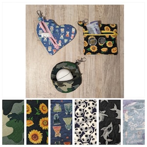 Könnte beinhalten: Ein Set aus acht verschiedenen Stoffdesigns für kleine Reißverschlusstaschen. Die Designs umfassen ein Herz mit einem Blumenmuster, einen schwarzen Hintergrund mit gelben Sonnenblumen, ein Tarnmuster, einen blauen Hintergrund mit einem weißen und blauen Blumenmuster, einen weißen Hintergrund mit schwarzen Fußbällen, einen schwarzen Hintergrund mit einem weißen Hai, einen blauen Hintergrund mit einem weißen Schneeflockenmuster und einen grünen Hintergrund mit einem Dinosaurier.