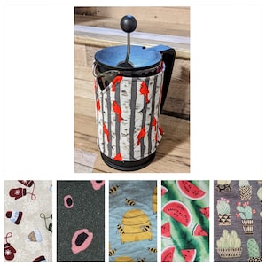 Peut inclure: Une cafetière à piston noire avec un couvercle amovible et une housse en tissu à motif de cardinal rouge et de bouleaux. La housse en tissu est un moyen confortable de garder votre café au chaud.