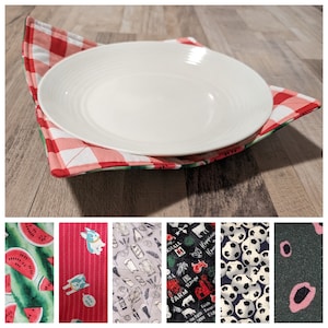 Może przedstawiać: Stojak na talerze z czerwono-białej kraty z białym ceramicznym talerzem w środku. Stojak jest wykonany z tkaniny i ma pikowany wzór. Talerz jest okrągły i ma lekko uniesiony brzeg.
