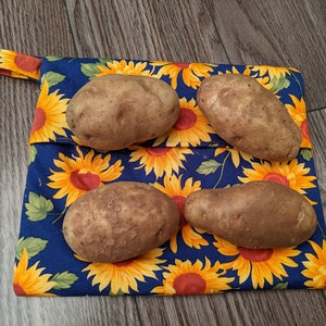 May include: A square fabric pouch featuring a vibrant sunflower pattern with yellow petals and green leaves on a dark blue background. Four raw brown potatoes are placed on top of the pouch, which includes a small fabric loop on the top left corner.