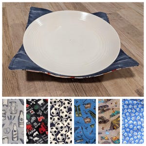 Puede incluir: Un plato de cerámica blanca descansa sobre un salvamanteles azul marino. El salvamanteles cuadrado está hecho de tela. Se muestran muestras de tela adicionales con varios patrones, incluyendo balones de fútbol, escenas de camping y diseños florales.