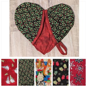 May include: A red heart-shaped oven mitt with a green and black floral print. The mitt has a red fabric lining and a black strap.