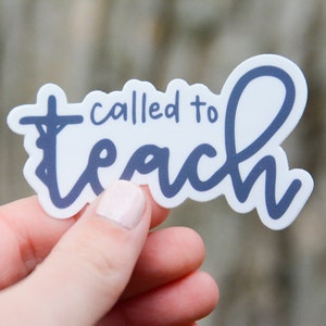 Pu&ograve; includere: Un adesivo bianco con la scritta "called to teach" in blu navy. La parola "teach" &egrave; scritta in un carattere script con un anello, e la lettera "t" in "called" &egrave; una croce. L'adesivo &egrave; tenuto da una persona.