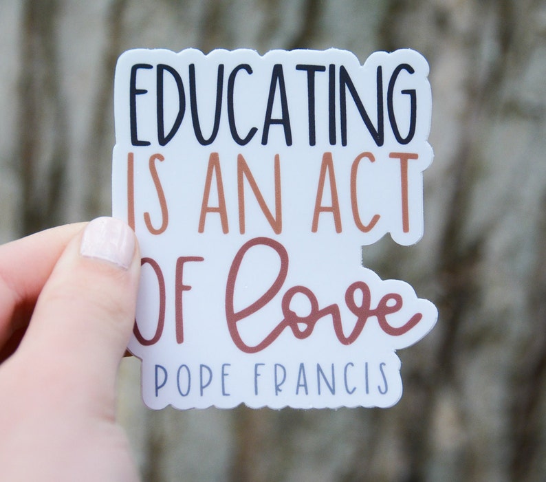 May include: White sticker with brown and black lettering that reads "Educating is an act of love Pope Francis".