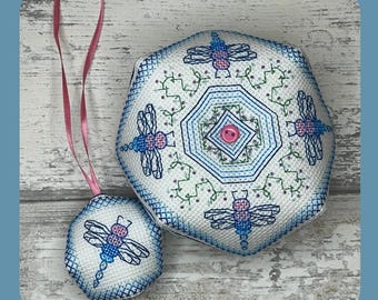 May include: A white cross-stitch pattern with a blue and pink dragonfly design. The pattern is on a round and octagonal piece of fabric. The fabric is attached to a pink ribbon. The text "PDF PATTERN" is at the bottom of the image.