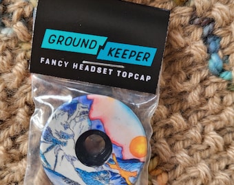 May include: A "GROUND KEEPER" fancy headset topcap in a clear plastic bag. The topcap features a mountain landscape design with blue, white, orange, and yellow colors. The topcap has a black center hole.