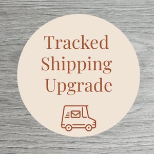 May include: A round sticker with the words "Tracked Shipping Upgrade" in brown text. Below the text is a brown illustration of a delivery truck with an envelope. The background is a light beige circle on a gray wood grain surface.