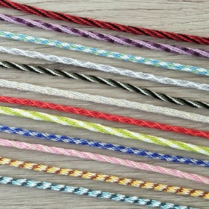 May include: Close-up of a collection of colorful twisted cords. The cords are in various colors, including red, purple, blue, green, and yellow. Each cord has a unique pattern and is made of a tightly woven material. The cords are arranged diagonally across a light wood surface.