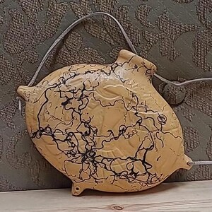 May include: A yellow ceramic gourd with black swirling patterns and a leather strap. The gourd has a rounded shape and a textured surface.
