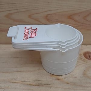 May include: White plastic measuring cups with the text "Betty Crocker" printed in red on the largest cup.