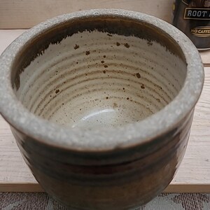 May include: A brown ceramic bowl with a white interior and a speckled glaze. The bowl has a rounded shape and a wide rim.