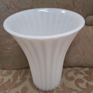 May include: A white ceramic vase with a fluted design. The vase is tall and narrow, with a wide opening at the top.