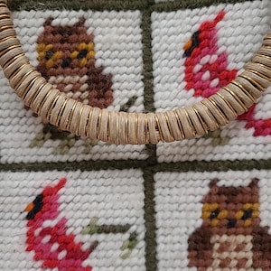 May include: A close-up of a woven, gold-colored handle with a white background. The background is a tapestry with a repeating pattern of red cardinals and brown owls.