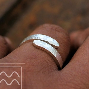 May include: A silver hammered wrap ring with a textured finish. The ring is open and adjustable to fit different finger sizes.